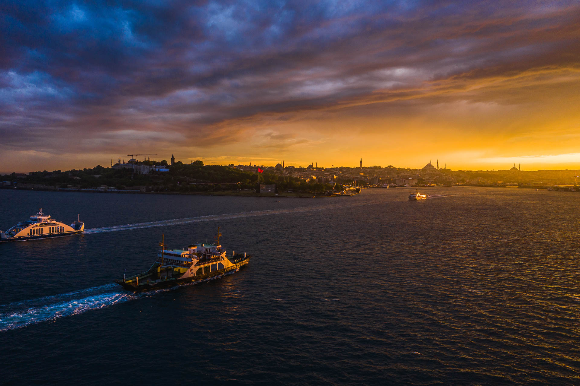 City ferries crossing the Bosphorus at sunset with the Istanbul skyline behind