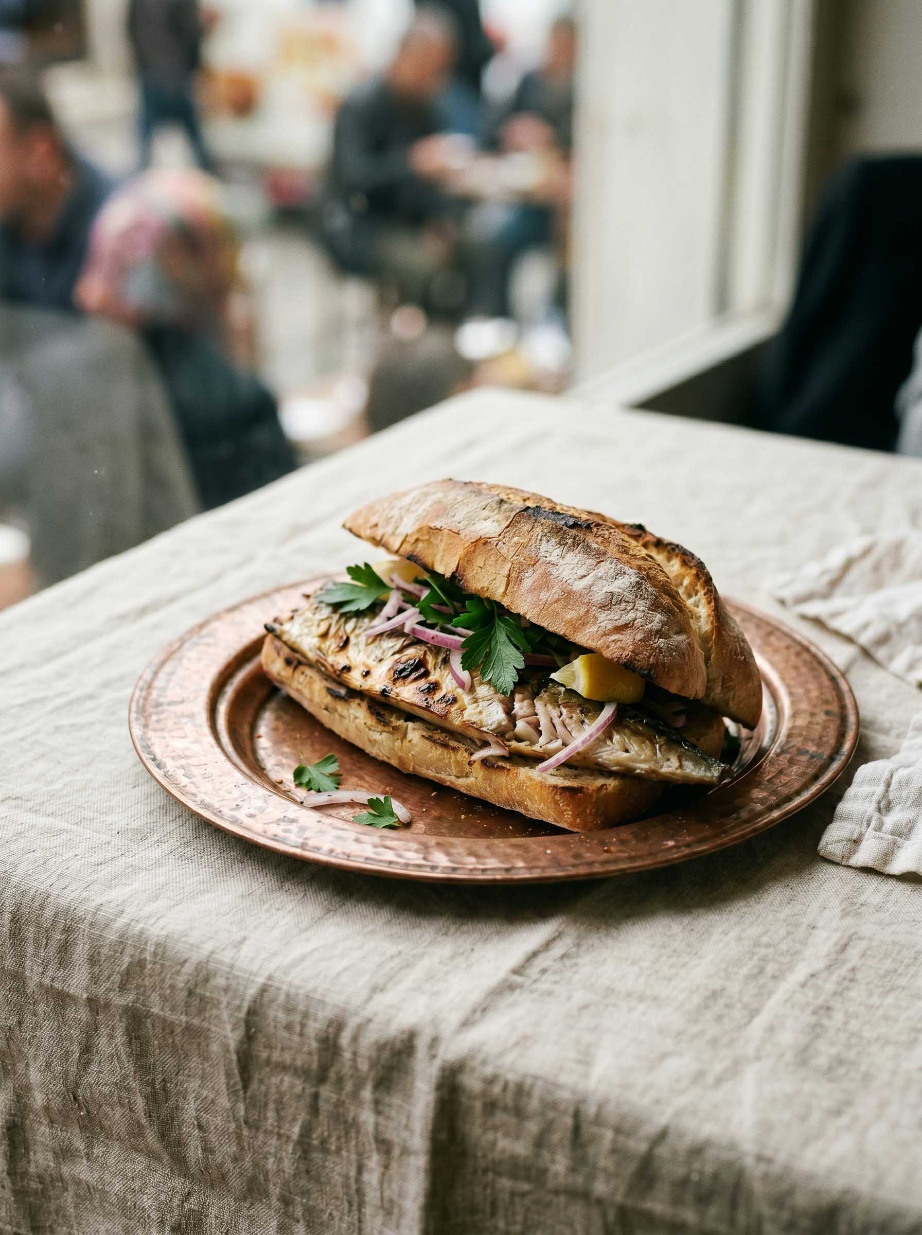 Balık ekmek, a grilled fish sandwich with onion and greens on a copper plate
